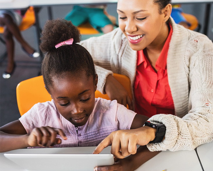 snapplify_cloud_services_pay_paragraph_image_1 - snapplify cloud services A teacher in a classroom, guiding a young child through a Teacha! classroom resource on a tablet device